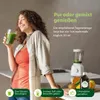 A woman is drinking a green smoothie in a kitchen setting, with a blender and fruits visible. Anteprima dell’immagine prodotto