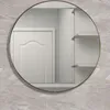 A round mirror with a gold frame is mounted on a tiled wall, reflecting a white door and shelves. Produktbild-Vorschau