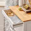 A kitchen cart with a wooden countertop, a partially open drawer containing utensils, and some fruit on the countertop. Produktbild-Vorschau
