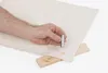 A hand holding a metal tool over a piece of fabric with a wooden block underneath. Produktbild-Vorschau