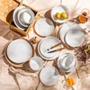 A collection of white ceramic plates and bowls arranged on a light pink tablecloth. Náhled obrázku produktu