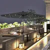 An outdoor patio setting at night with tables, chairs, and umbrellas illuminated by LED lights. Produktbild-Vorschau