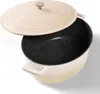 A cream-colored oval cocotte with a black speckled interior and a partially open lid, set against a white background. Produktbild-Vorschau