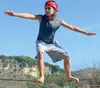 A young person is balancing on a slackline outdoors with a blue sky and hills in the background. Produktbild-Vorschau