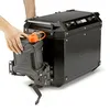 A person's hands are shown attaching a black jerrycan holder with an orange-capped jerrycan to a black aluminum motorcycle pannier. Produktbild-Vorschau