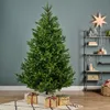 A Christmas tree decorated with gifts at its base, in a room setting with shelves in the background. Podgląd zdjęcia produktu