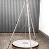 A tripod grill stand with a circular grill plate, set up outdoors on a paved surface. Anteprima dell’immagine prodotto