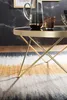 A close-up shot of a modern coffee table with a glass top and gold metal legs, placed on a rug with an abstract pattern. A glass pitcher and a glass are on the table. Náhľad obrázku produktu