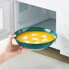 A hand is placing a bowl of soup into a microwave. Produktbild-Vorschau
