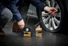 A person is using a tire sealant kit to repair a car tire on a wet road. Produktbild-Vorschau