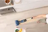 A person is using a blue and black wet and dry vacuum cleaner on a light-colored wooden floor in a kitchen setting. Podgląd zdjęcia produktu