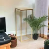 A gold metal plant stand with a potted plant next to it, in a room with a TV and curtains. Náhľad obrázku produktu