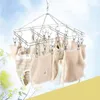 A stainless steel sock dryer with multiple clips hangs against a sky background, with some yellow flowers in the foreground. Produktbild-Vorschau