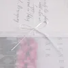 A close-up of a white fabric with handwritten text and a pink floral pattern, tied with a white ribbon. Produktbild-Vorschau