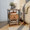 A bedside table with books and a vase of flowers next to a sofa with a blanket. Produktbild-Vorschau