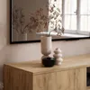 A close-up view of a wooden TV cabinet with decorative items on top, including vases and a bowl, with a mirror reflecting the scene in the background. Produktbild-Vorschau