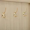 Three gold coat hooks mounted on a light wood panel. Podgląd zdjęcia produktu