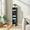 A tall, narrow black shelf unit filled with CDs and some books, placed in a bright room next to a large window with sheer curtains and a large potted plant. Náhled obrázku produktu