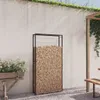 An outdoor patio scene with a firewood rack filled with wood, a planter with flowers, and a wooden bench under a pergola. Produktbild-Vorschau