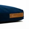 A close-up of a navy blue dog bed with a brown leather tag. Produktbild-Vorschau