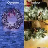 A split image showing Christmas wreaths decorated with lights, one displayed outdoors on a stone wall and the other indoors on a shelf. Produktbild-Vorschau