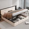 A beige upholstered bed with its storage compartment open, revealing folded linens and other items. Produktbild-Vorschau