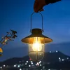 A hand holding a solar lantern at dusk with a city skyline in the background. Produktbild-Vorschau