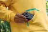 A person is putting a compact camera into the pocket of a yellow hoodie. Podgląd zdjęcia produktu