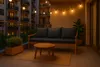 A balcony at dusk with a sofa, coffee table, and string lights. Produktbild-Vorschau