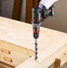 A person wearing a glove is using a cordless drill with a large auger bit to drill into a wooden workbench. Podgląd zdjęcia produktu