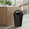A hand is shown throwing trash into a black trash can in a kitchen or dining area. Náhľad obrázku produktu