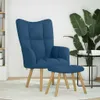A blue fabric armchair and matching ottoman are placed on a light-colored rug in a room with a bookshelf and a large potted plant.