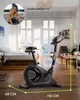 An exercise bike is shown in a room with a bed and furniture, with a person in the upper left corner. Produktbild-Vorschau