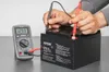 A person is testing a battery with a multimeter. Anteprima dell’immagine prodotto