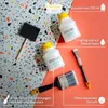 Two bottles of varnish, a sponge brush, and two paintbrushes are arranged on a background split between a terrazzo pattern and a solid coral color. Produktbild-Vorschau