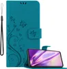 A teal flip phone case with a floral and butterfly design is shown open, with a smartphone inside. A black wrist strap is attached to the left side of the case. Voir les images du produit