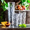 A still life arrangement of glasses, fruit, and greenery on a wooden surface. Náhled obrázku produktu