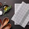 A flat lay of kitchen items including a bowl of olive oil with rosemary, salt, peppercorns, a dried chili pepper, wooden salad servers, and folded checkered kitchen towels. Anteprima dell’immagine prodotto