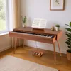 A digital piano is set up in a room with a window and a plant. Produktbild-Vorschau