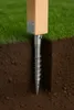 A wooden post secured by a metal screw-in ground anchor, shown in a cross-section of soil and grass. Produktbild-Vorschau