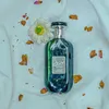 A bottle of perfume is placed on a white fabric with dried flower petals scattered around it. Náhľad obrázku produktu