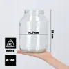 A hand holding a clear glass jar with measurement indicators. Voir les images du produit