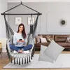 A woman is sitting in a hanging chair indoors, holding a phone. Produktbild-Vorschau
