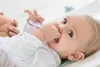 A baby is lying on its back and chewing on a pacifier. Produktbild-Vorschau