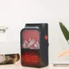 A small electric heater with a realistic flame effect is placed on a table next to a rolled-up magazine. A hand is reaching towards a laptop in the background. Anteprima dell’immagine prodotto