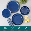 A set of blue ceramic plates and bowls arranged on a light gray surface, with a small plant in the background and lemons and a glass of water in the foreground. Voir les images du produit