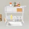 A white dish drying rack is set up over a white sink, with various kitchen items like bottles, a food processor, dishes, and cleaning supplies displayed on it. Podgląd zdjęcia produktu