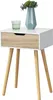 A white and wood-tone side table with a drawer, a glass of water, and a vase with greenery on top. Náhled obrázku produktu