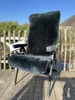 A dark gray sheepskin chair cover is draped over a folding chair on a wooden deck. Produktbild-Vorschau