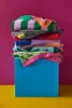 A stack of colorful beach towels on a blue cube against a magenta background. Produktbild-Vorschau